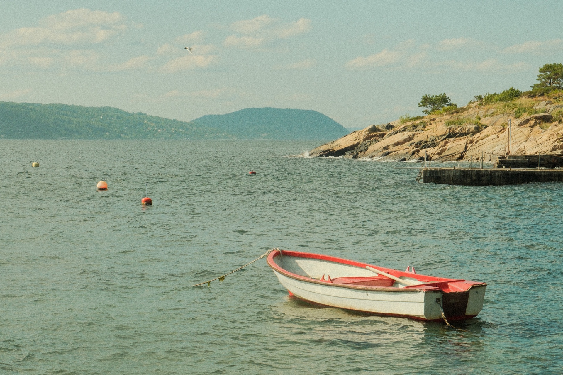 A small red and white rowing boat moored in the calm fjord at Hvitsten.
