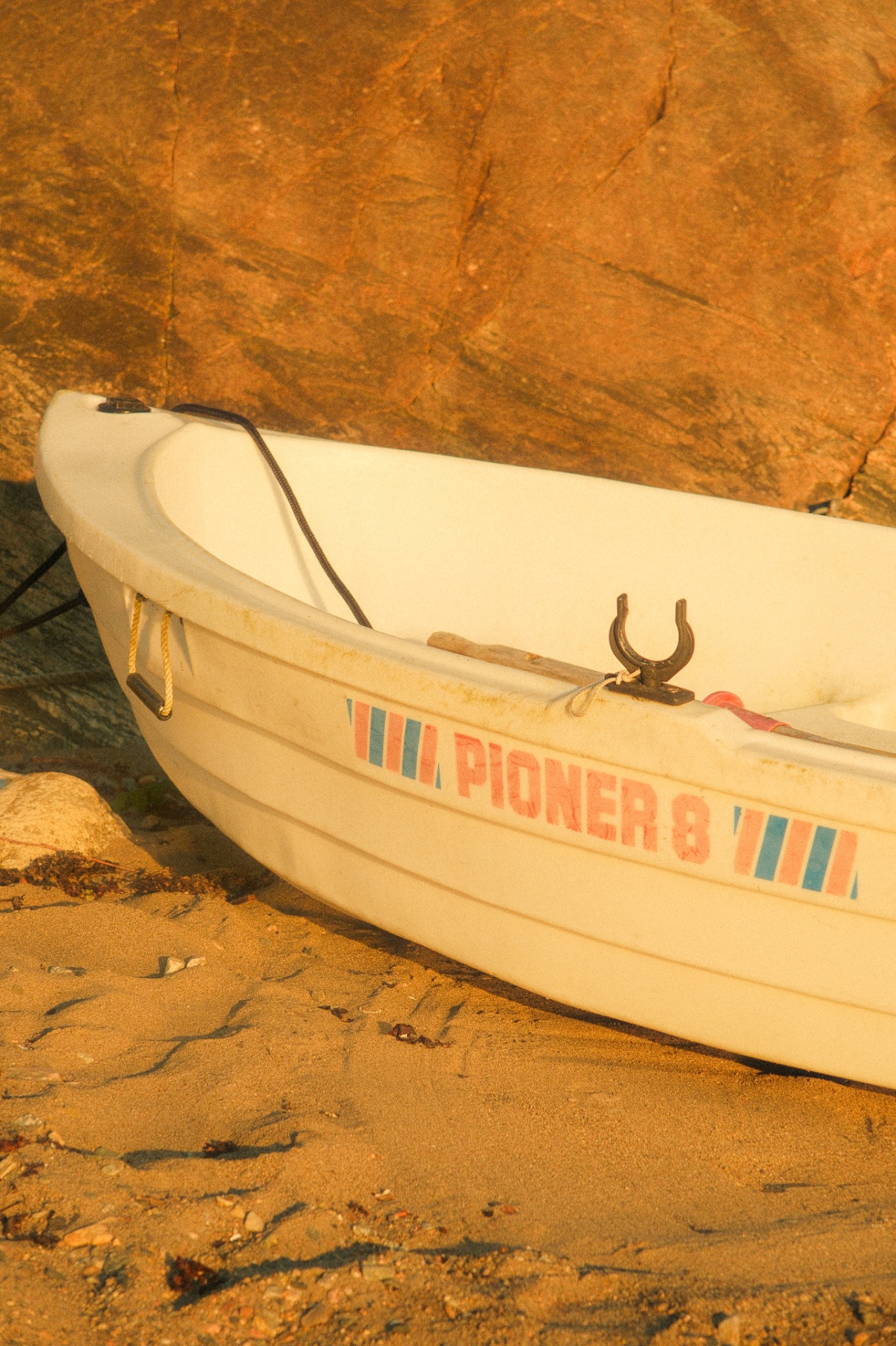 A white Pioner rowing boat pulled up on the rocky shore in golden hour light.