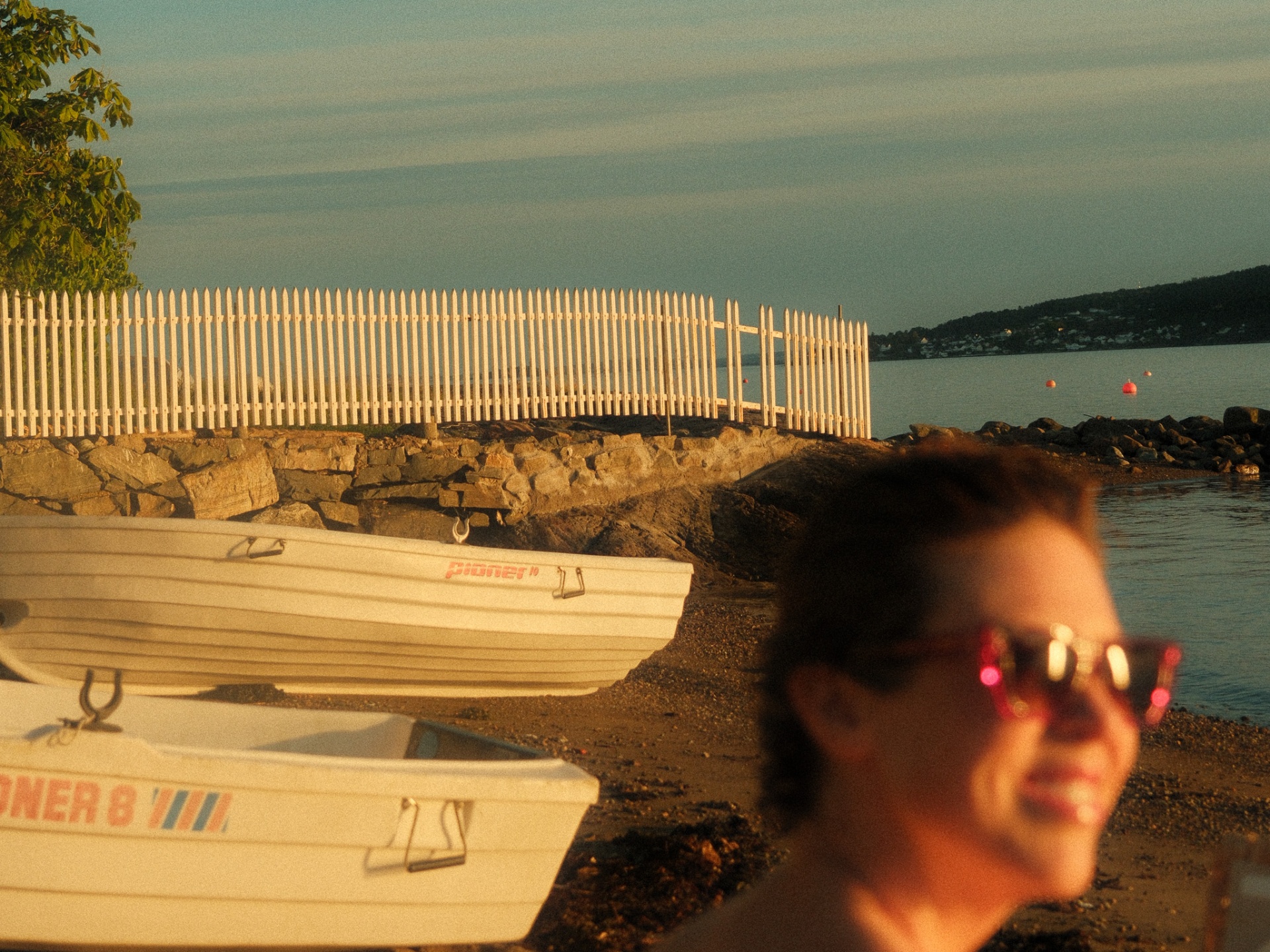 Pioner boats and a white picket fence by the water in Hvitsten at sunset.
